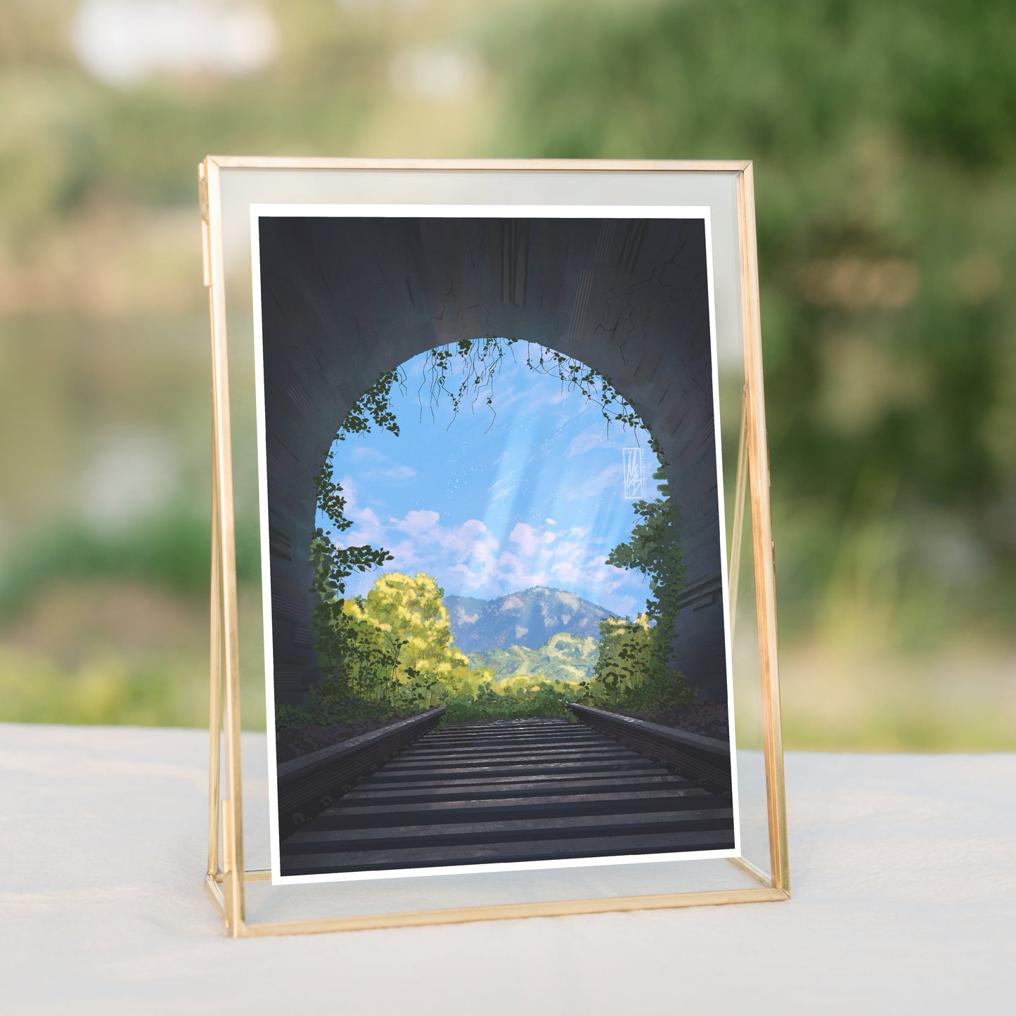 Framed artwork of a scenic path with trees and sky, placed on a surface outdoors.